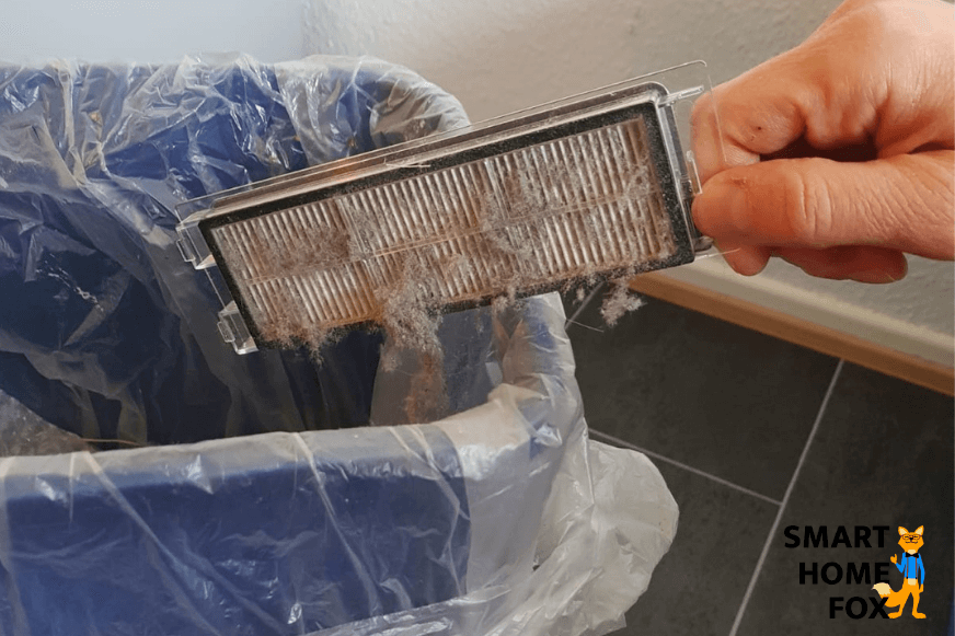 Der HEPA-Filter wird über einem Mülleimer ausgeklopft 